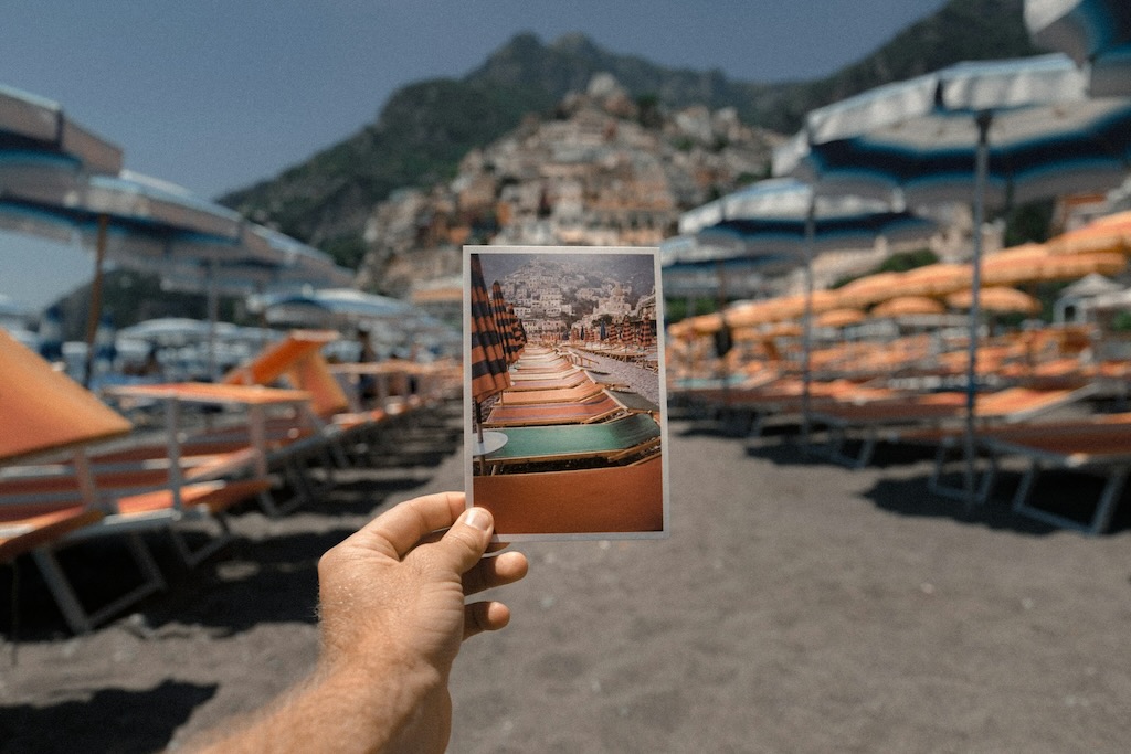 Person holding a vacation photo on the beach the photo was taken at